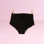 Black high-waisted underwear hanging on a clothesline against a pink background